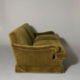 A large traditionally upholstered sofa covered in an olive-green mohair velvet, piped with green linen.