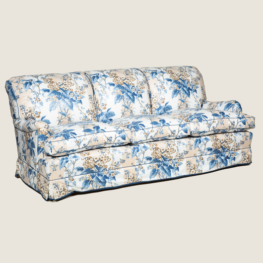 A large three seat sofa in a traditional style upholstered in a floral chintz fabric in blues and browns on a white ground.