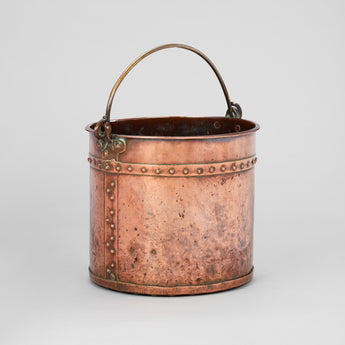 AN EARLY 20TH CENTURY COPPER BUCKET WITH RIVET AND STRAP DETAILS AND A BRASS CARRYING HANDLE.