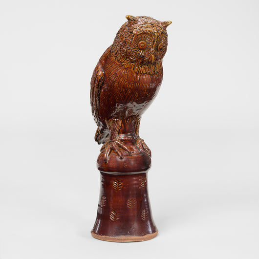 A POTTERY OWL FIGURINE IN A BROWN GLAZE, PERCHED ON A STAND