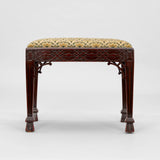 AN EDWARDIAN STOOL WITH A FRETWORK DECORATED FRAME, TAPERING LEGS AND A NEEDLEPOINT PANEL TO THE TOP.