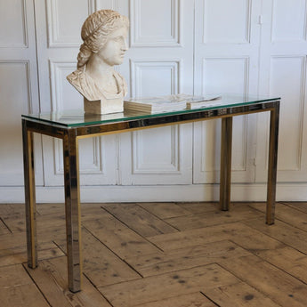 A 1970s ITALIAN CONSOLE TABLE DESIGNED BY RENATO ZEVI FOR ROMEO REGA. THE SIMPLE CHROME BASE SET OFF WITH AN INNER GOLD DETAIL AND WITH A GLASS TOP.