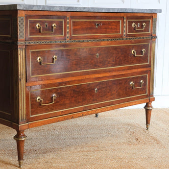 A FINE LOUIS XVI PERIOD MAHOGANY COMMODE WITH BRASS MOUNTS, INSET BRASS REEDED PILATERS AND EBONY AND BRASS CORNER PANELS, WITH A GREY MARBLE TOP.
