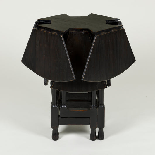 An ebonised early 20th century round oak table with 8 segmental drop-leaves on a four gate-leg base.