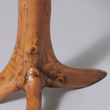 A small rustic table, the top of a cross-section of a yew tree trunk and the base three branches.