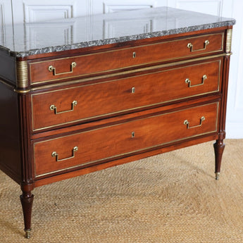 A 19TH CENTURY THREE-DRAWER MAHOGANY COMMODE IN THE LOUIS XVI TASTE, WITH A GREY MARBLE TOP AND BRASS MOUNTS.