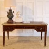 AN EARLY 20TH CENTURY FRENCH MAHOGANY DESK WITH REEDED LEGS, FLAME MAHOGANY VENEERED PANELS, BRASS MOUNTS AND ORIGINAL LEATHER TOP.