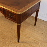 AN EARLY 20TH CENTURY FRENCH MAHOGANY DESK WITH REEDED LEGS, FLAME MAHOGANY VENEERED PANELS, BRASS MOUNTS AND ORIGINAL LEATHER TOP.