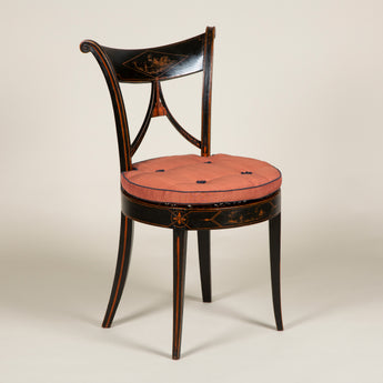 A pair of elegant ebonised side chairs with rounded splayed backs. The top rail painted with rural scenes within a lozenge, and round caned seats. Probably Italian, circa 1810.
