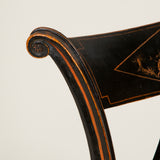 A pair of elegant ebonised side chairs with rounded splayed backs. The top rail painted with rural scenes within a lozenge, and round caned seats. Probably Italian, circa 1810.