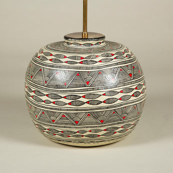 A pot-bellied papier mache pot with red and black geometric decoration on a white ground. Wired as a lamp.