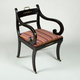 A regency ebonised elbow chair with a caned seat, sabre legs and brass mounts 1810.