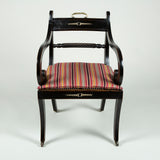 A regency ebonised elbow chair with a caned seat, sabre legs and brass mounts 1810.