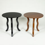 Low round teak tables with serpentine legs in a polished or an ebonised finish.