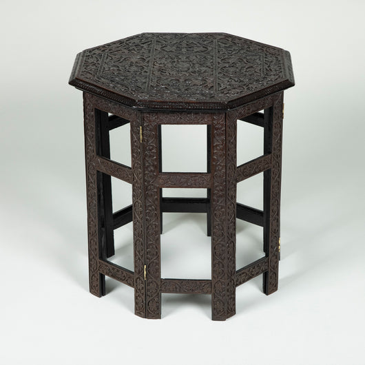 A small octagonal densely-carved hardwood table with folding base, probably Indian late 19th/early 20th century.