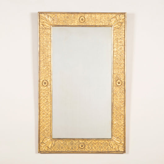 A late 19th early 20th century rectangular giltwood and composition mirror, the wide flat frame embossed with a dense patter of flowerheads and with acanthus leaf corners.