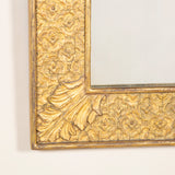 A late 19th early 20th century rectangular giltwood and composition mirror, the wide flat frame embossed with a dense patter of flowerheads and with acanthus leaf corners.