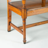 A stylish early 19th century long elmwood settle with a triple ladder back and elegant turned legs.