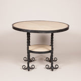A round wrought iron table, the top and small round under-tier inset with bleached mahogany and the four legs each with four scrolled feet. Probably French, mid-20th century.
